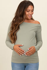woman wearing a light green off-the-shoulder maternity top and holding her baby bump