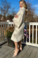 woman wearing a cream maternity coat and holding her baby bump while standing on a porch