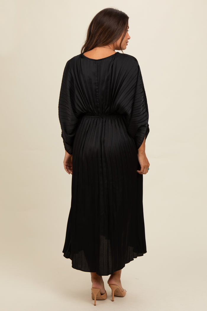 woman wearing a black pleated maternity maxi dress with a cinched waist and long sleeves, showing a baby bump from behind
