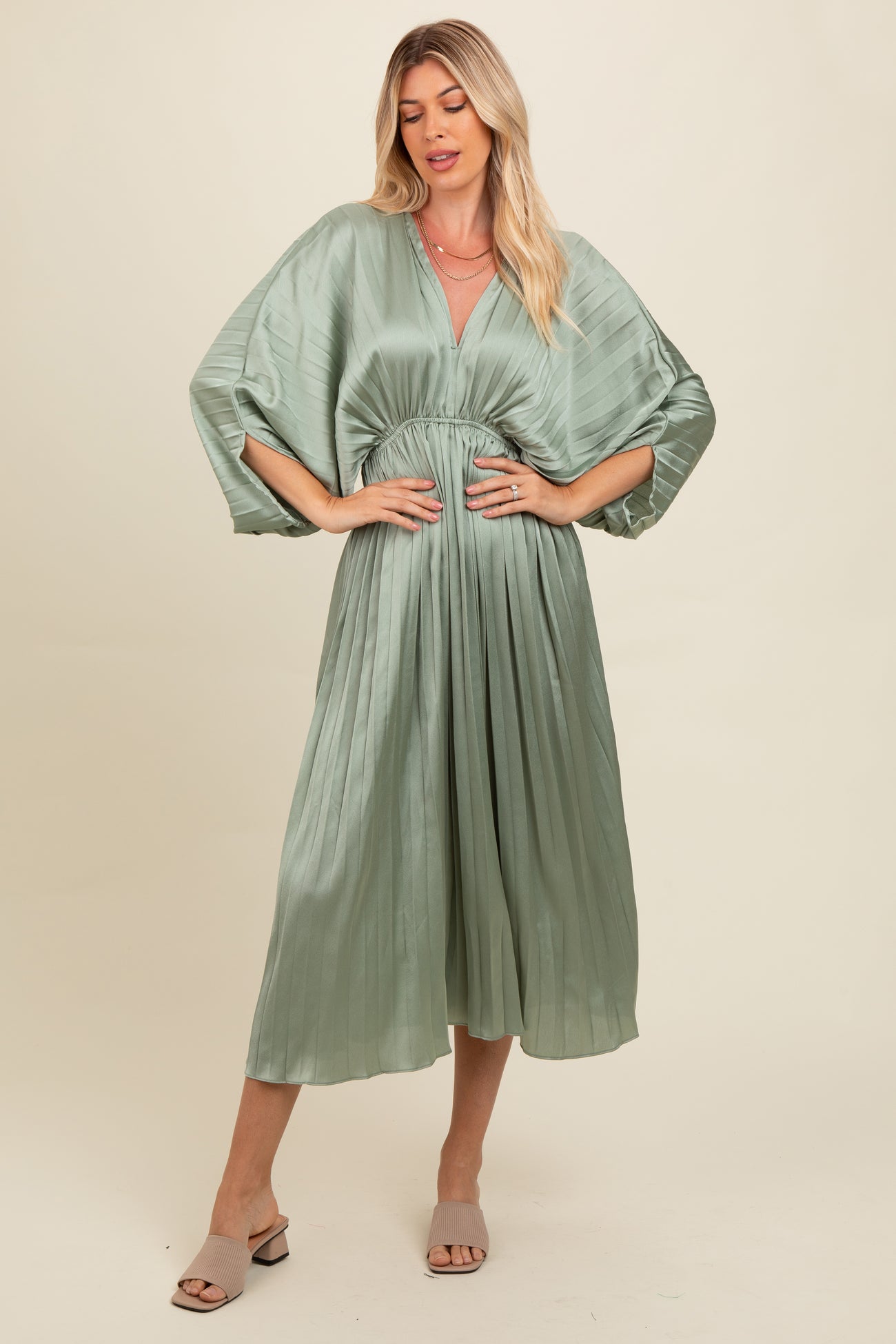 woman wearing a light green pleated maxi dress with a deep V-neck and wide sleeves, styled with open-toe mules