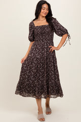 woman wearing a dark floral midi dress with puff sleeves and tie details on the sleeves, standing on a neutral background