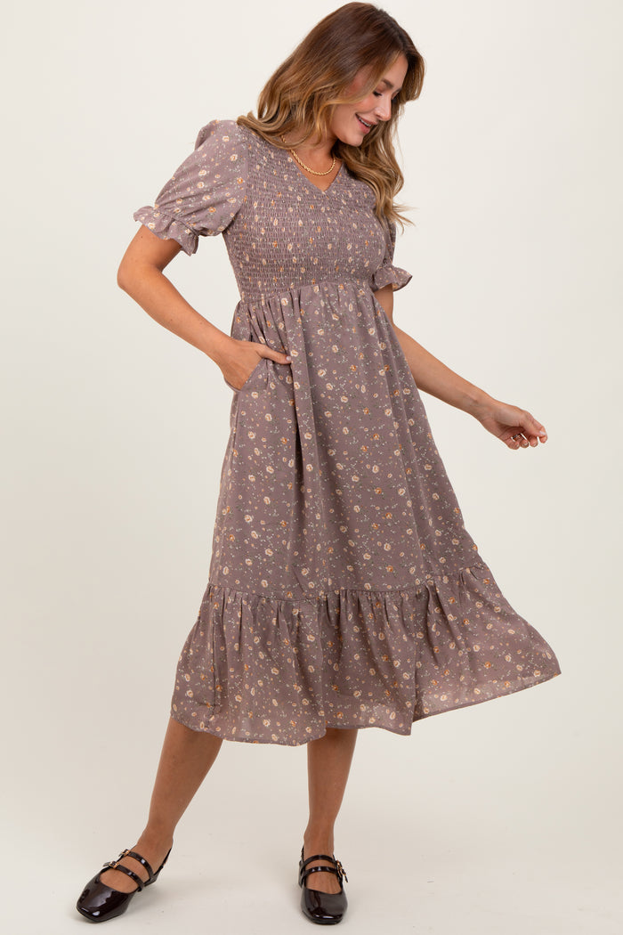 woman wearing a brown floral midi dress with puff sleeves and pockets, smiling while standing to the side