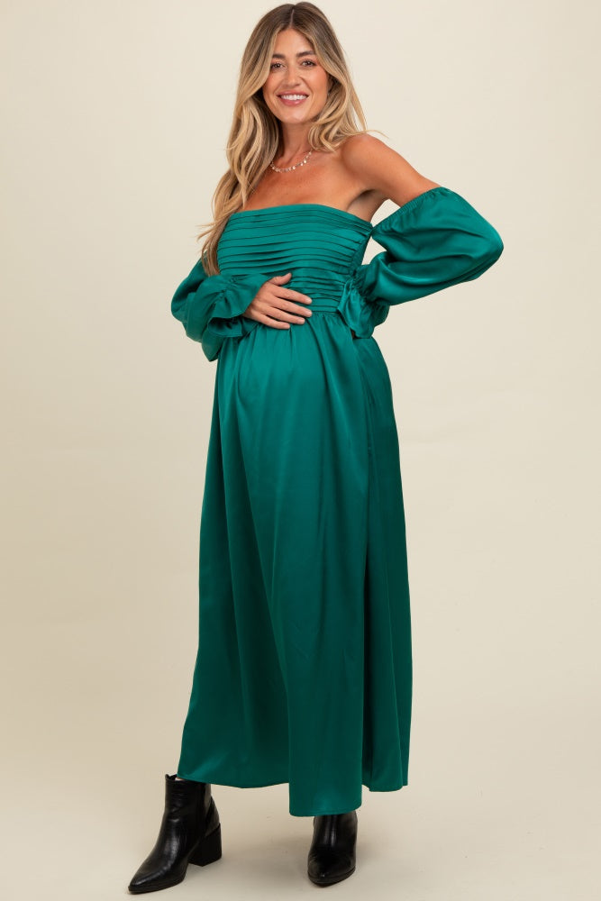 woman wearing a dark green off-the-shoulder maternity dress with puff sleeves, holding her baby bump
