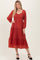 woman wearing a rust red long sleeve maxi dress with a tiered skirt and v-neckline, posing against a neutral background