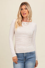 woman wearing a light beige long sleeve top with gathered detailing and a crew neckline, paired with blue denim jeans
