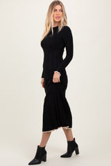 woman wearing a black ribbed midi dress with long sleeves and a scalloped hem, paired with black ankle boots