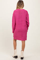 woman wearing a vibrant pink oversized maternity sweater dress, seen from the back, paired with white ankle boots