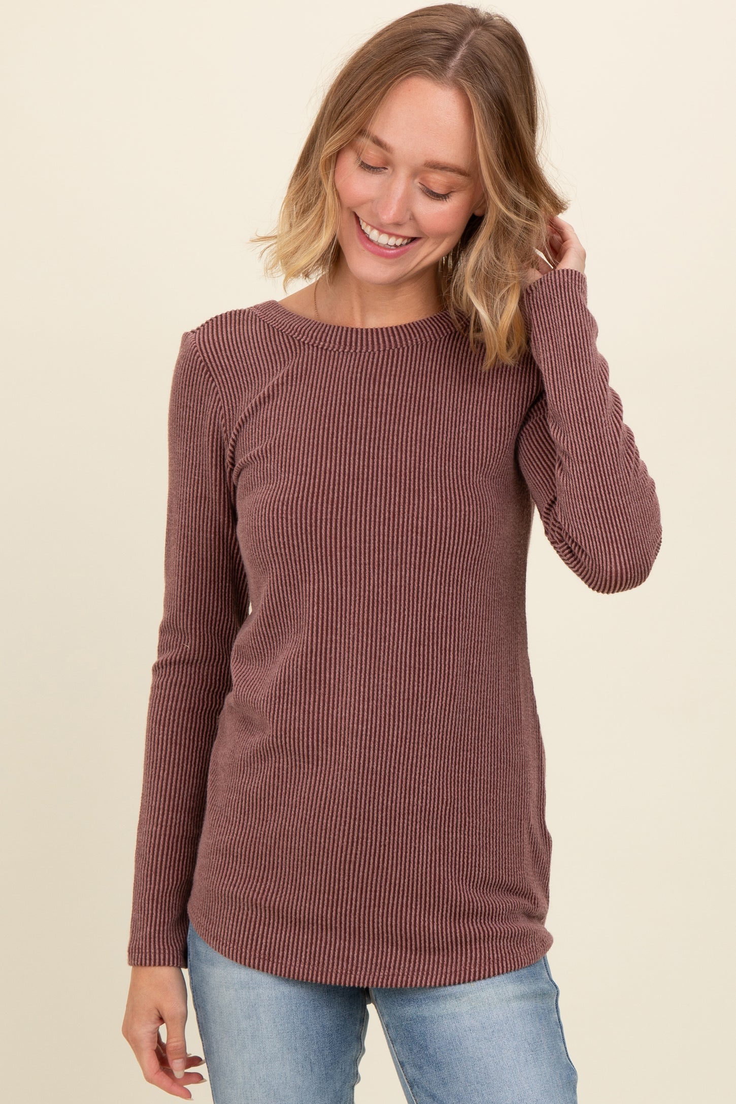 woman wearing a maroon long sleeve ribbed top and smiling with one hand in her hair