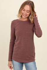 woman wearing a maroon long sleeve ribbed top and smiling with one hand in her hair