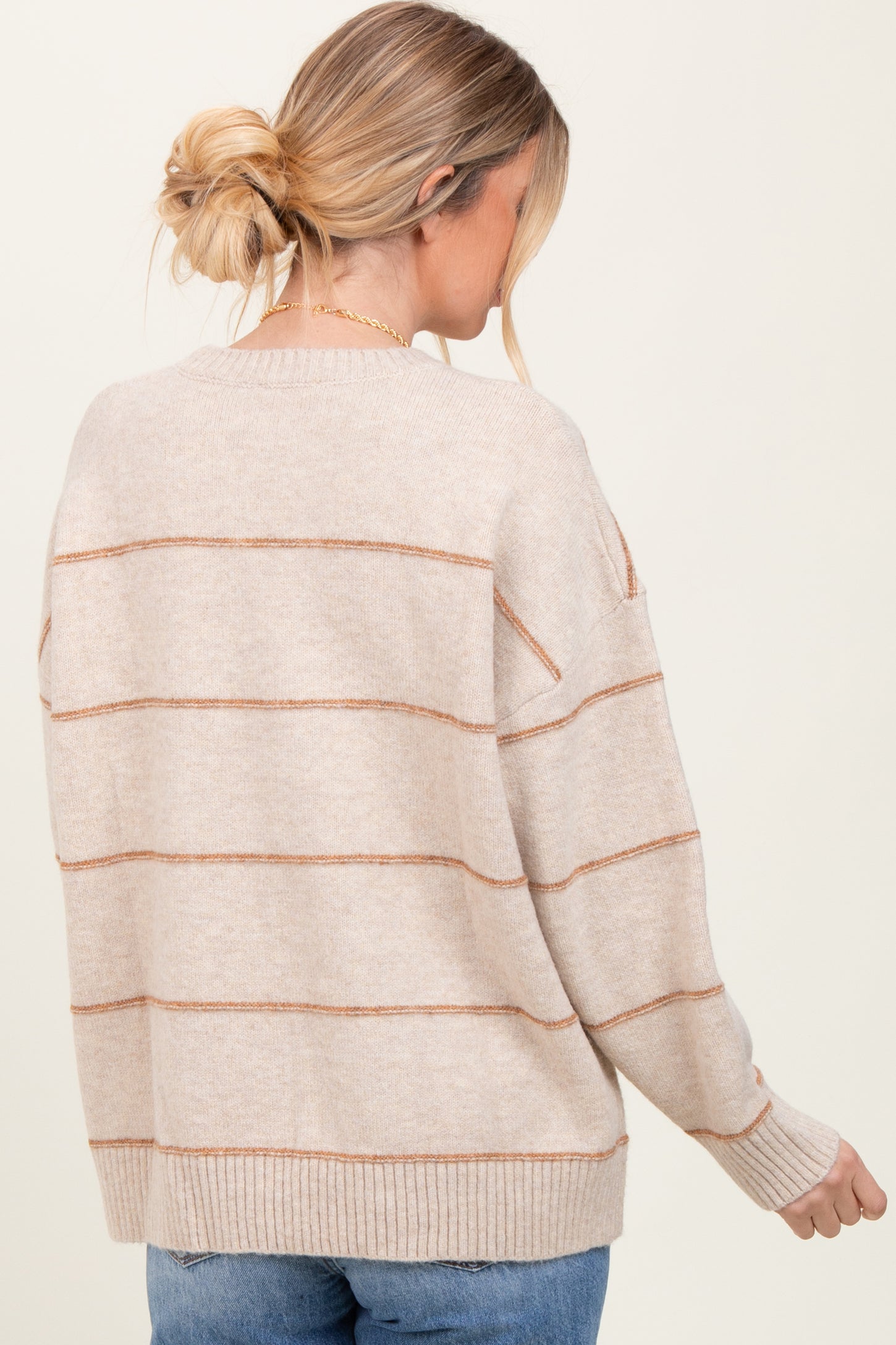 woman wearing a beige striped sweater with a relaxed fit and ribbed hem, seen from the back