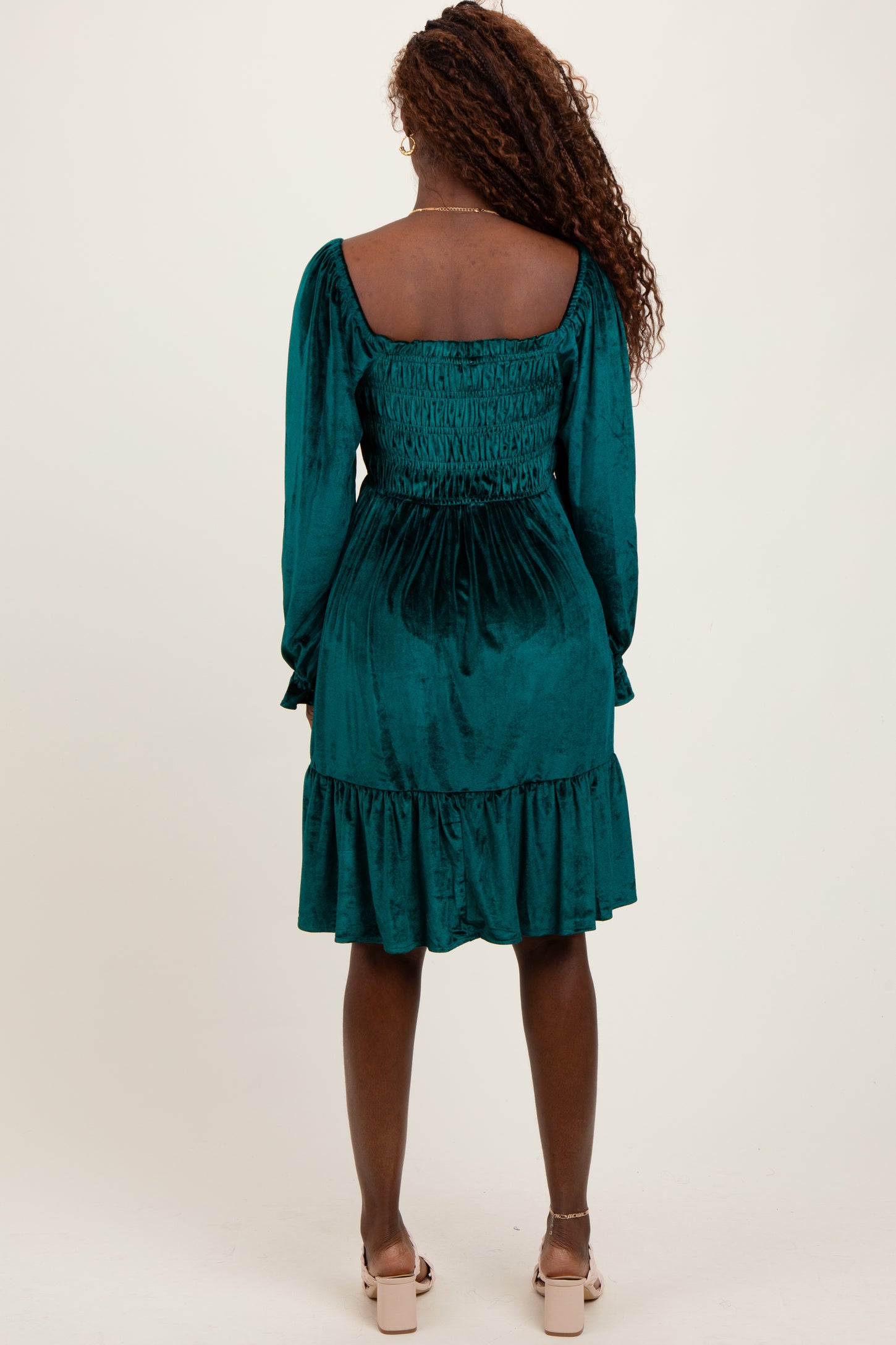 woman wearing a teal velvet smock dress with long sleeves and a ruffled hem, viewed from the back