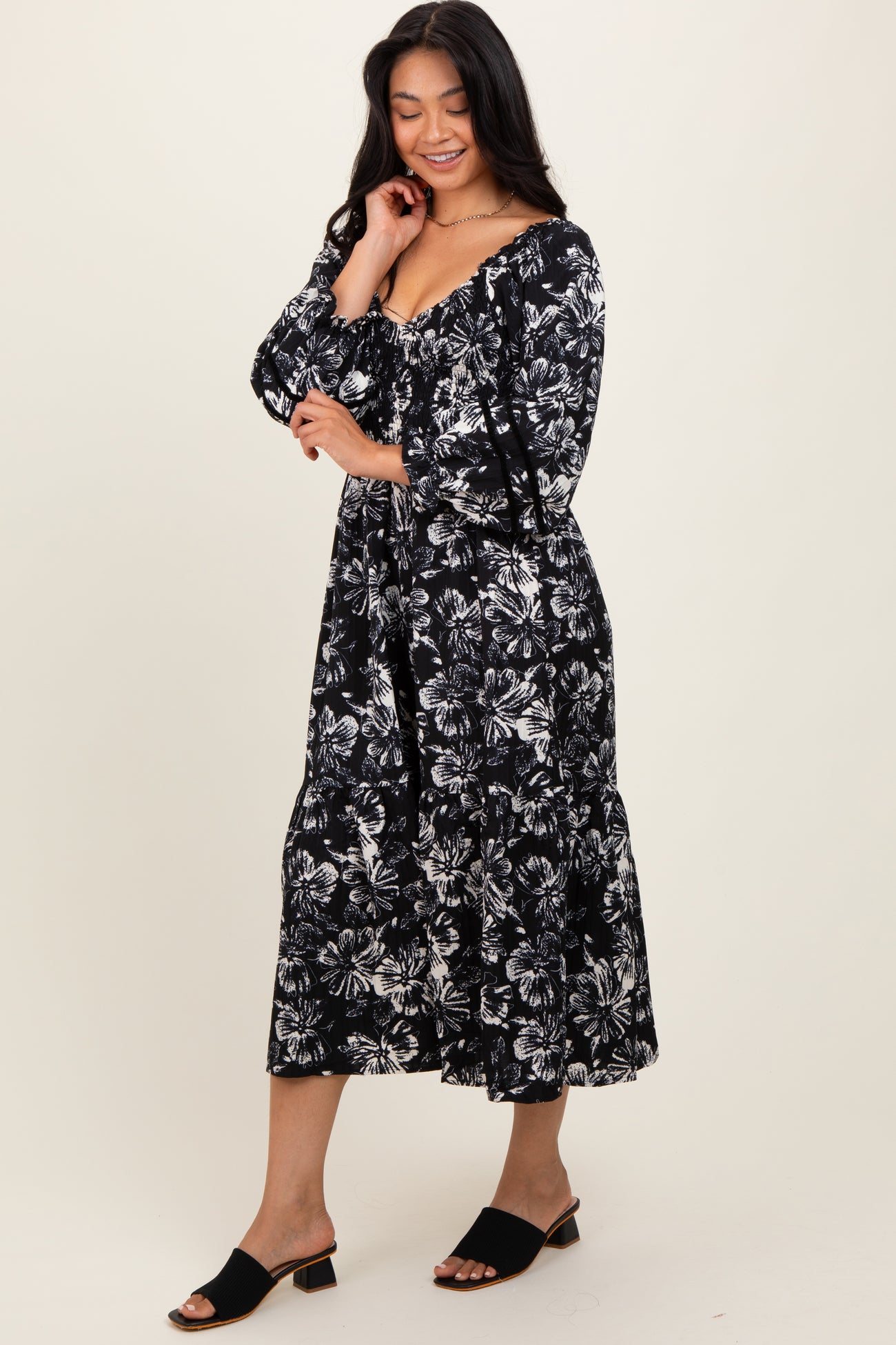 woman wearing a black and white floral maxi dress with a v-neckline and long sleeves, standing on a light background