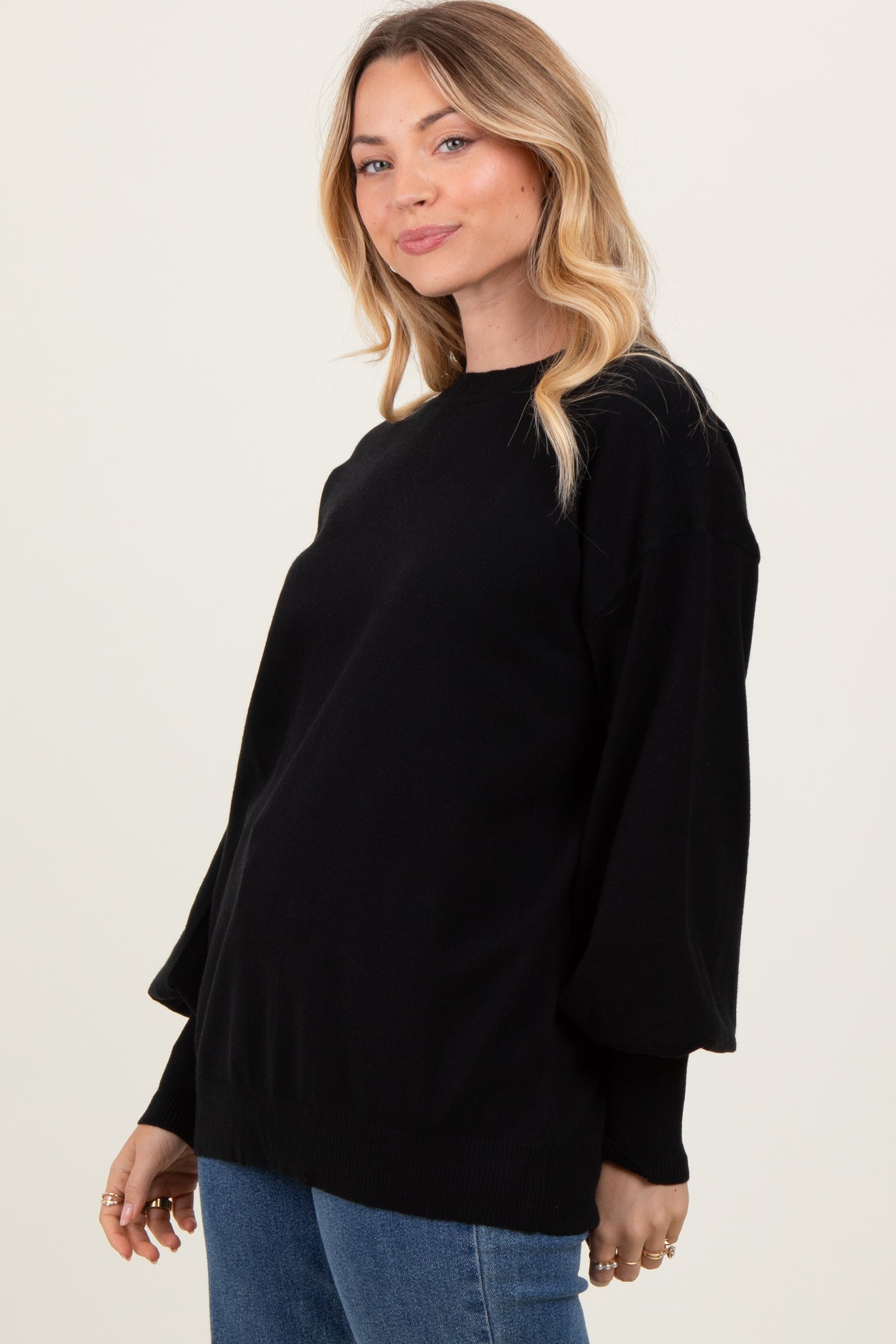 woman wearing a black oversized sweater with puff sleeves and a rounded neckline, paired with blue jeans