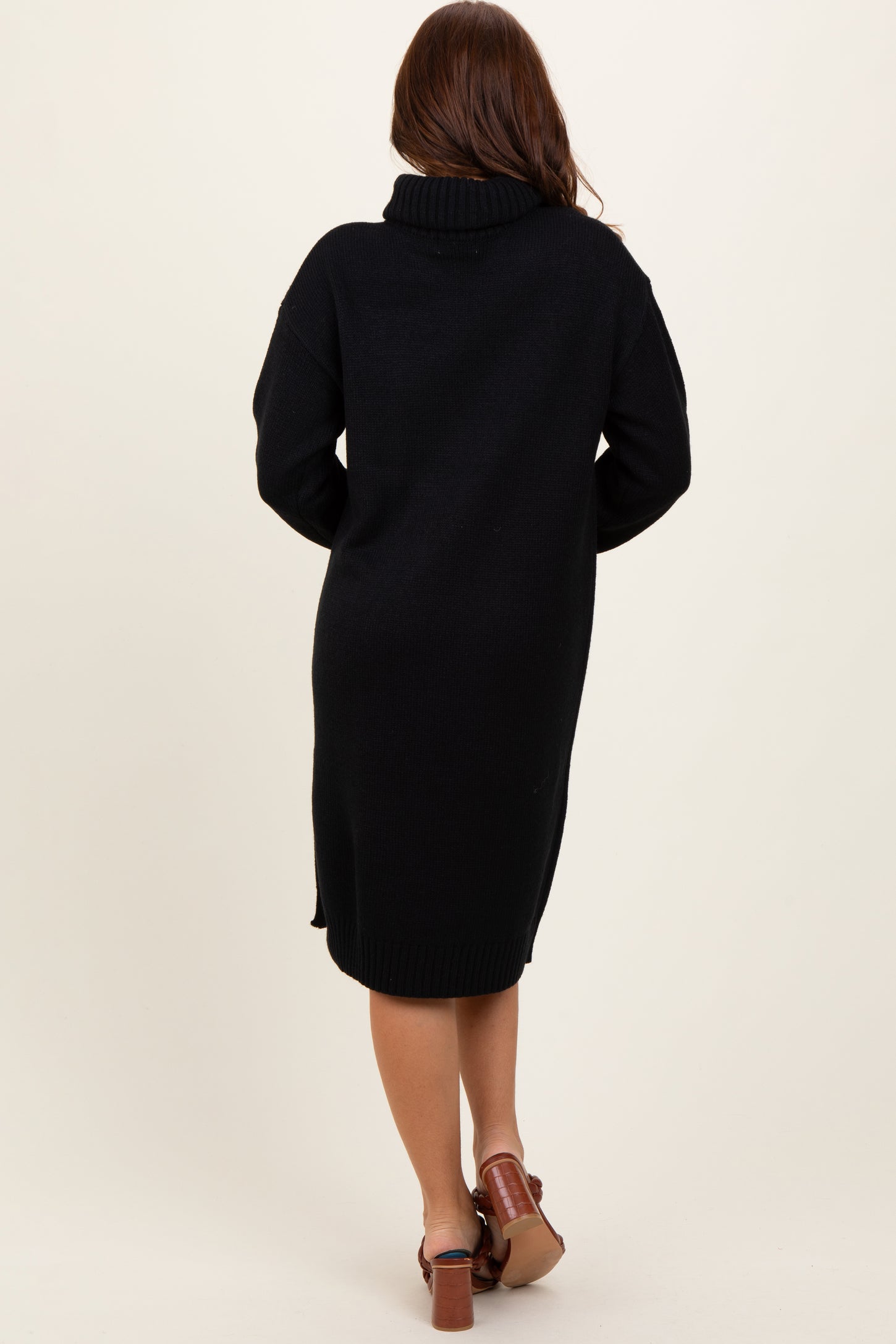 woman wearing a black long sleeve knitted sweater dress with a high neck and side slits