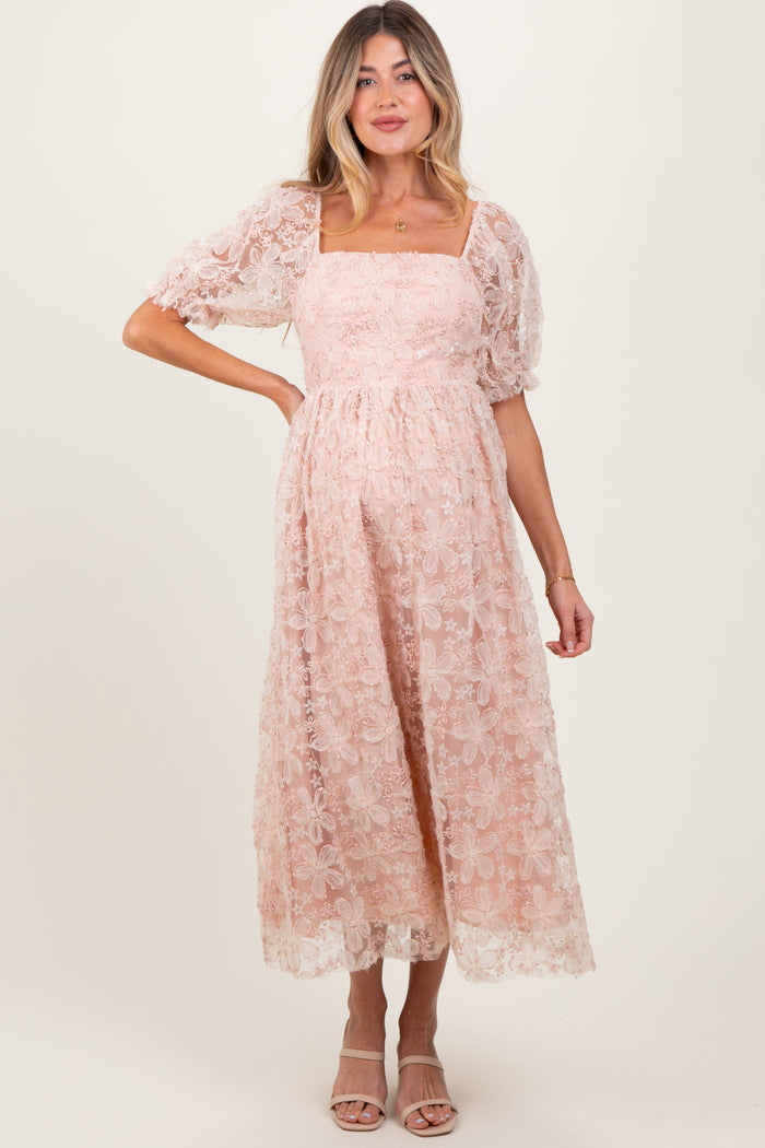 woman wearing a blush pink floral lace maternity dress with puff sleeves and a square neckline, showing her baby bump