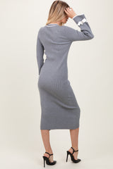 woman wearing a form-fitting gray ribbed long sleeve dress with white ruffle details on the sleeves and high heels