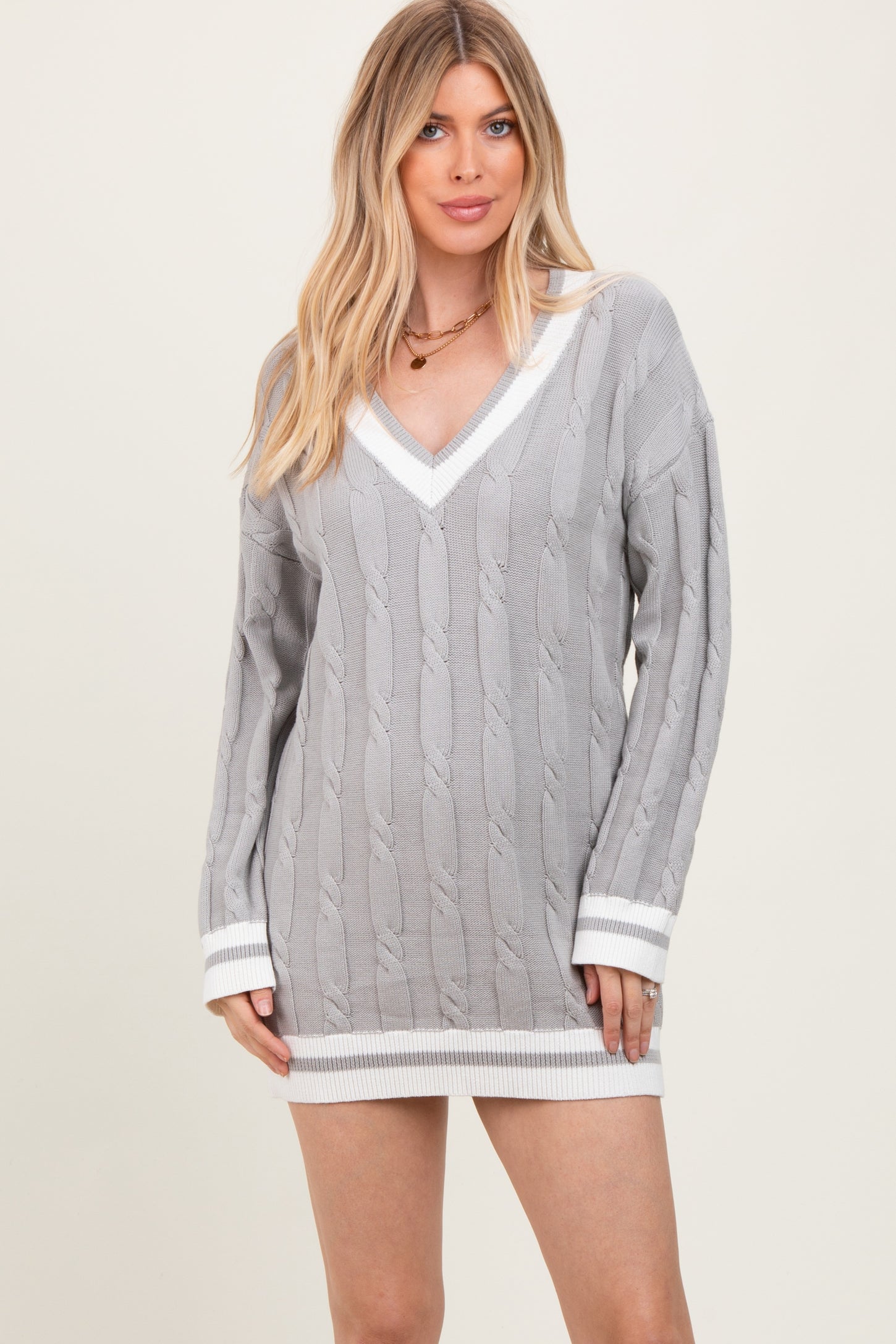 woman wearing a gray cable-knit mini sweater dress with white trim and a deep v-neckline