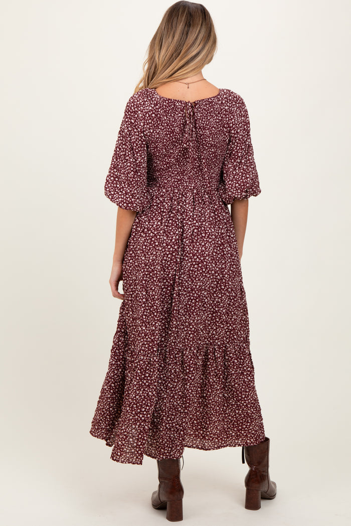 woman wearing a burgundy floral maternity maxi dress with short puff sleeves and a tiered skirt, showing the back view