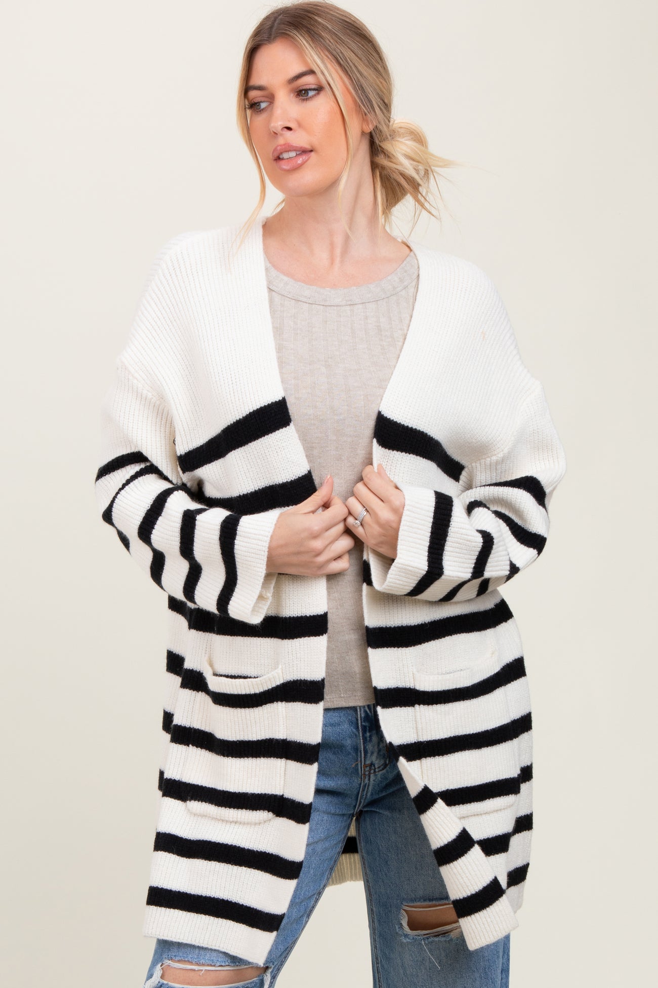 woman wearing a cream and black striped oversized cardigan over a beige sweater and distressed jeans