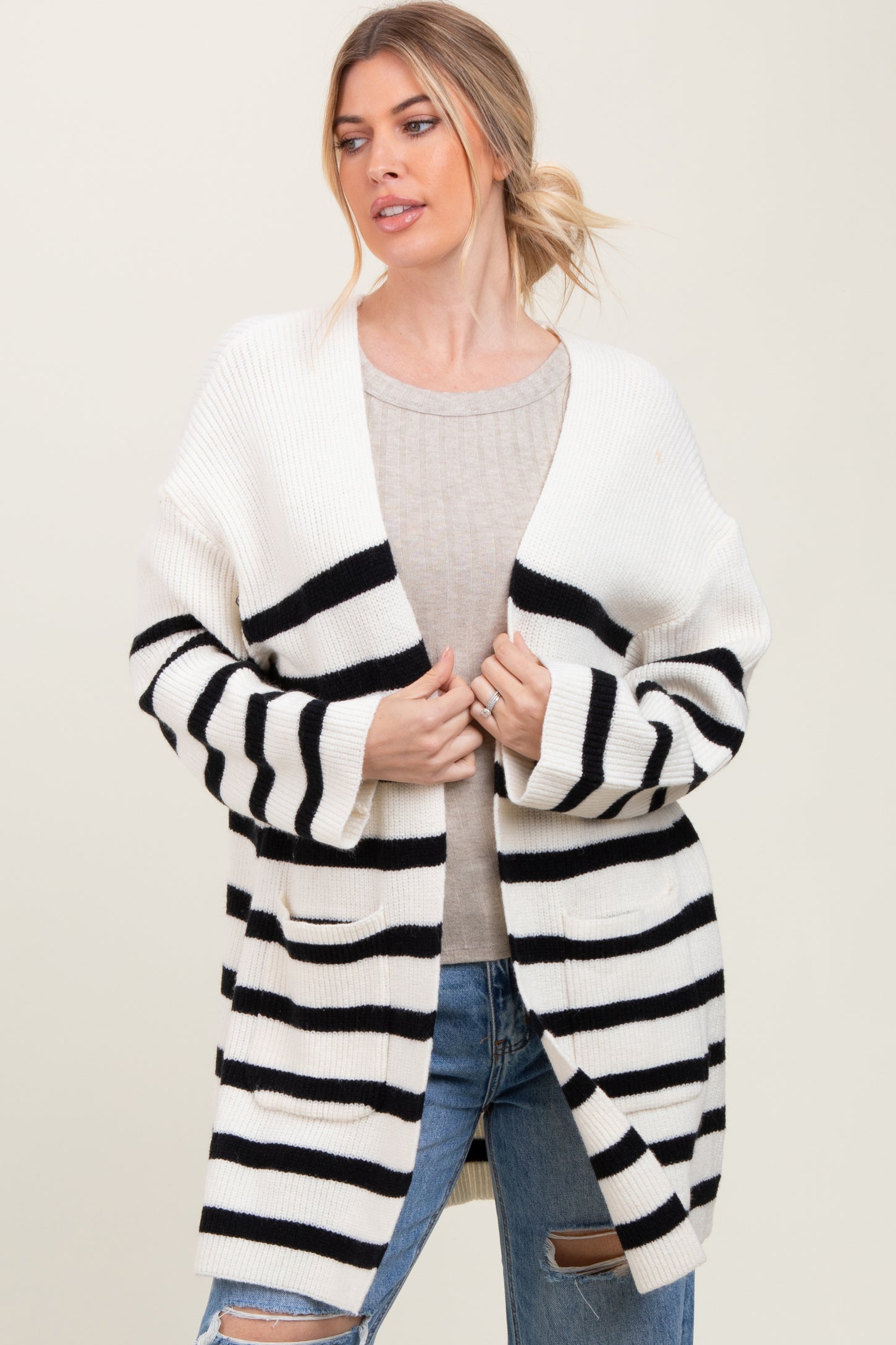 woman wearing a cream and black striped oversized cardigan over a beige sweater and distressed jeans