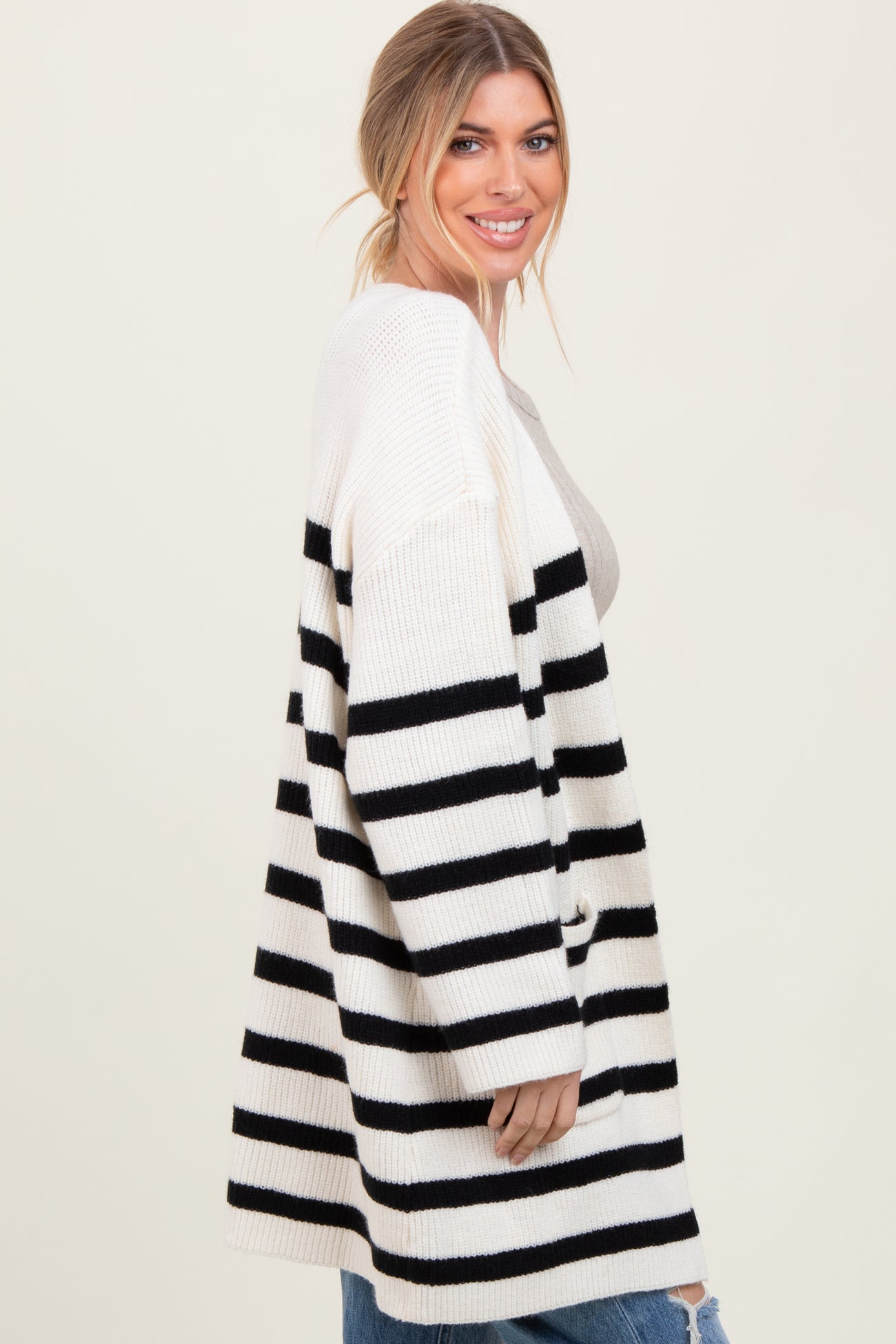 woman wearing a cream and black striped oversized cardigan, smiling, with distressed jeans and a light top underneath
