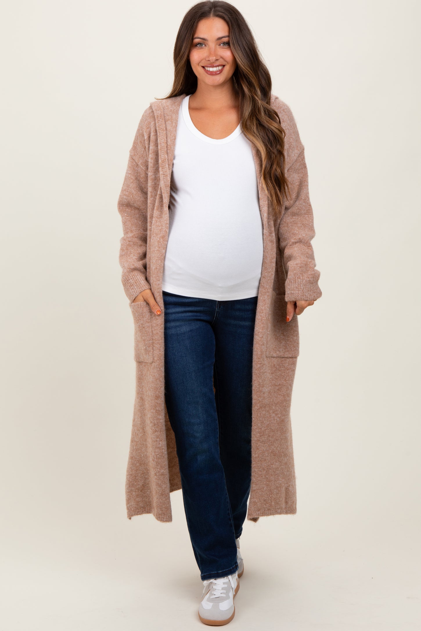 woman wearing a cozy beige maternity cardigan over a white top and jeans, showing her baby bump