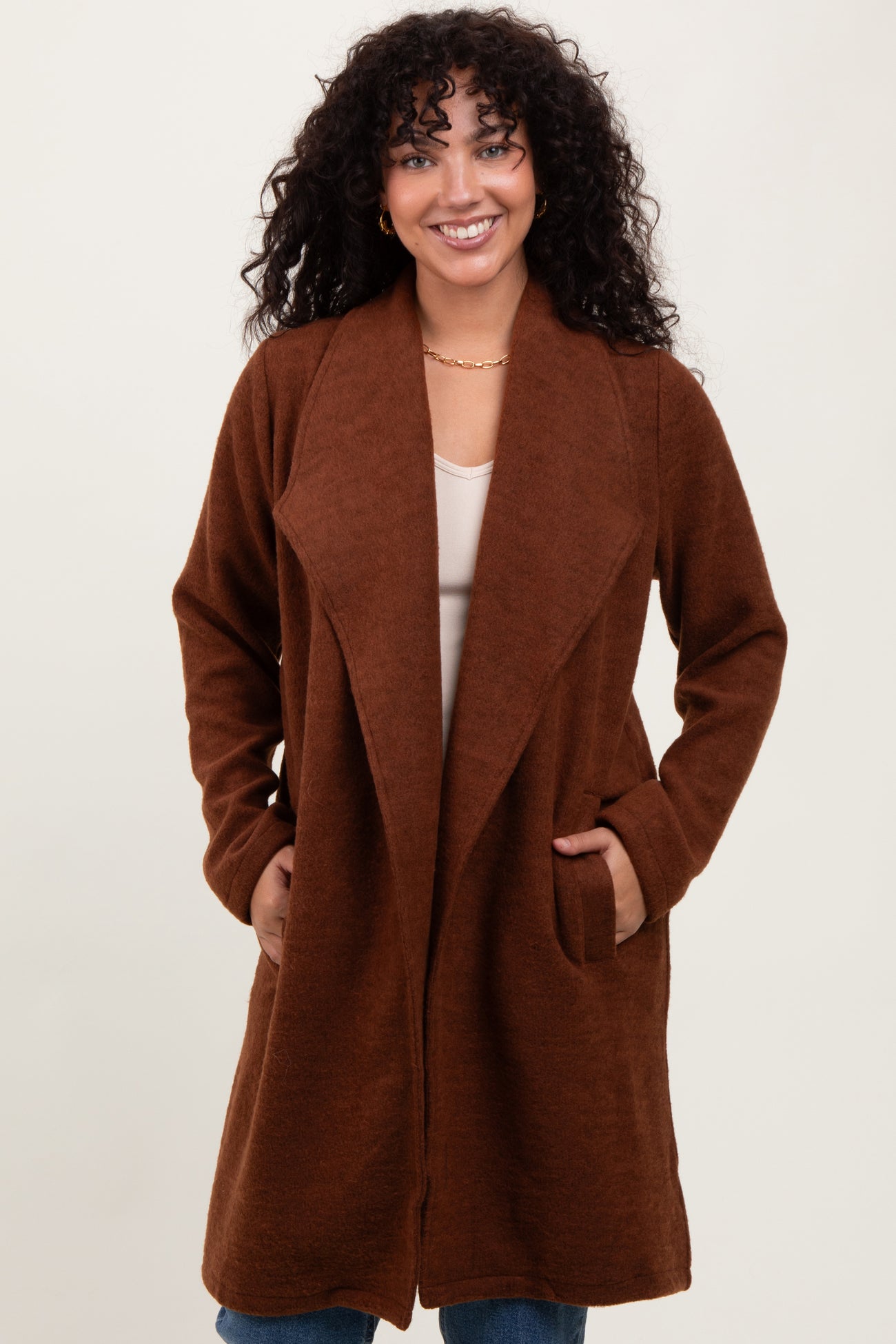 woman wearing a brown long cardigan with an open front and pockets, smiling at the camera