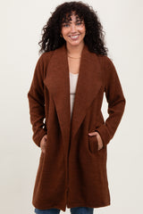 woman wearing a brown long cardigan with an open front and pockets, smiling at the camera