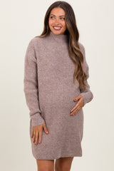 woman wearing a loose-fitting taupe maternity sweater dress, smiling and gently holding her baby bump