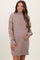 woman wearing a loose-fitting taupe maternity sweater dress, smiling and gently holding her baby bump