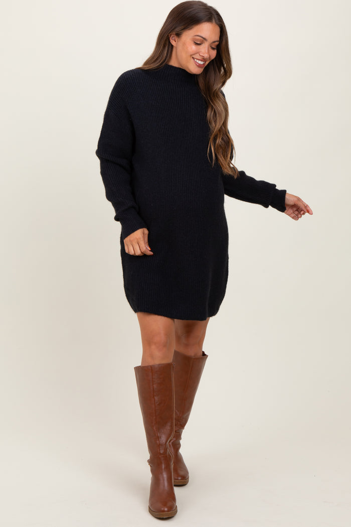 woman wearing a black knitted maternity sweater dress with long sleeves and knee-high brown boots, showcasing her baby bump
