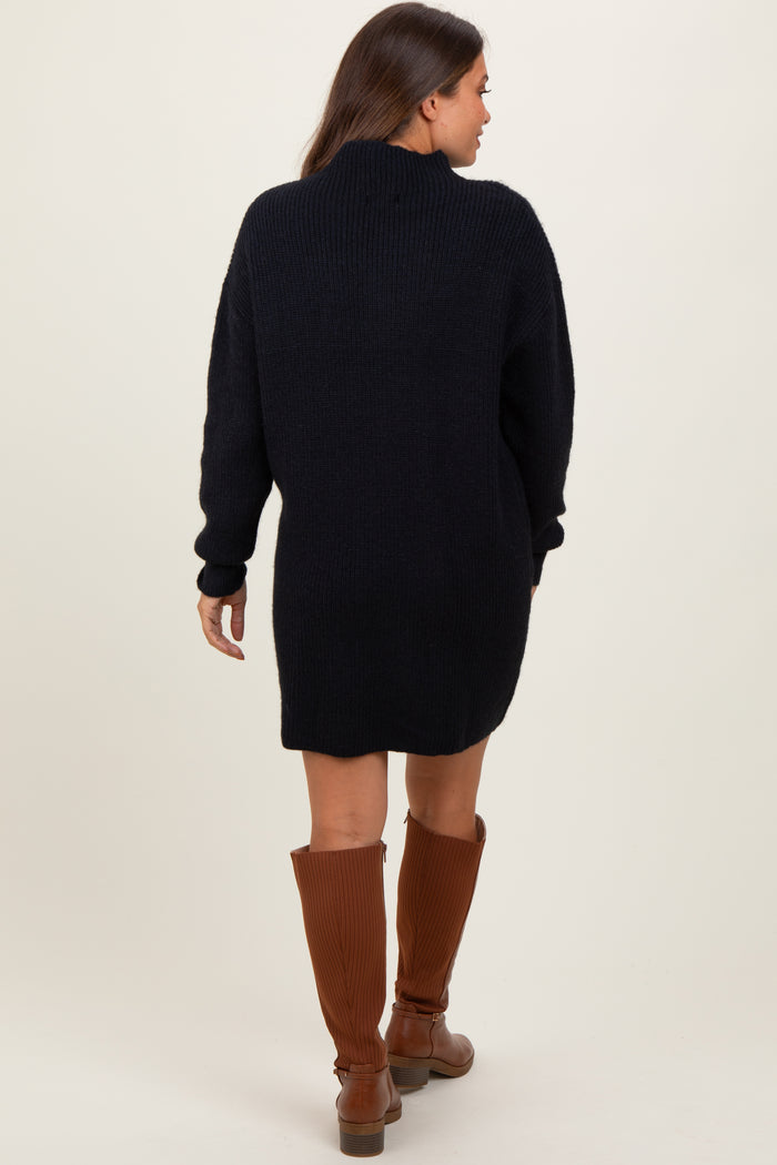 woman wearing a navy blue oversized knit maternity sweater dress viewed from the back, paired with brown knee-high boots