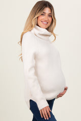 woman wearing a cream turtleneck maternity sweater, showing her baby bump, styled with blue jeans