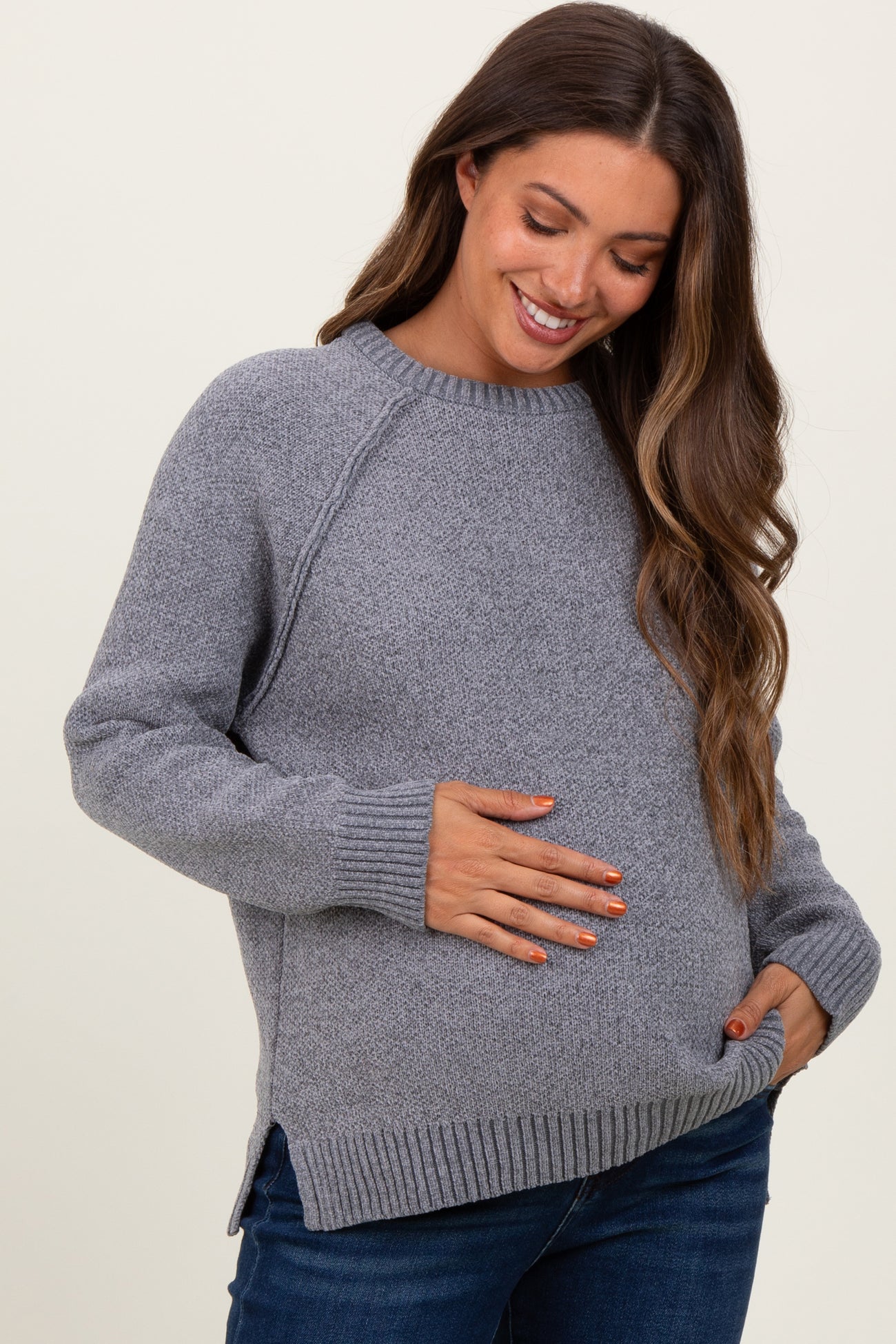 woman wearing a gray maternity sweater with ribbed hem and side slits, holding her baby bump