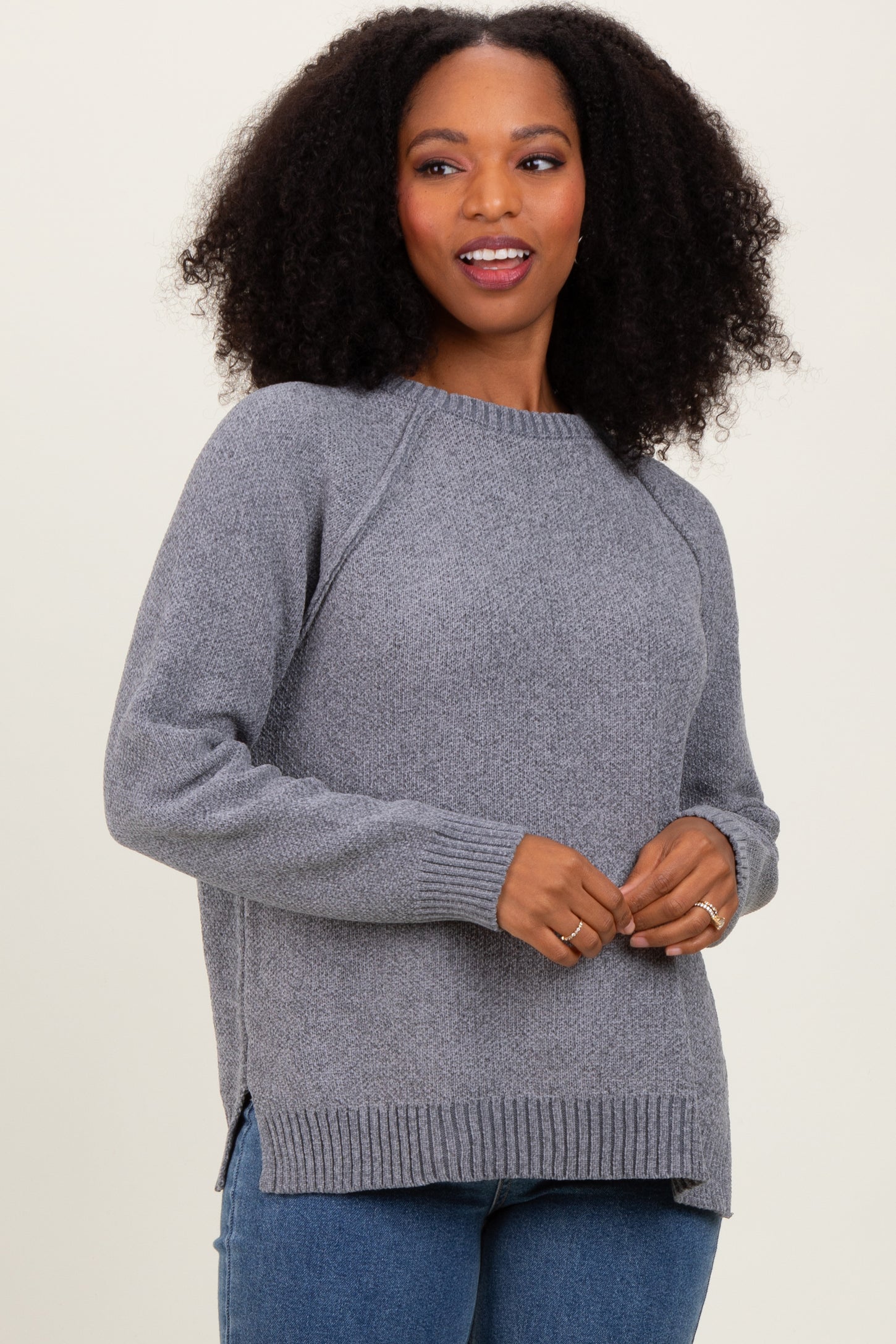 woman wearing a gray long sleeve sweater with side slits and ribbed hem, styled with blue jeans