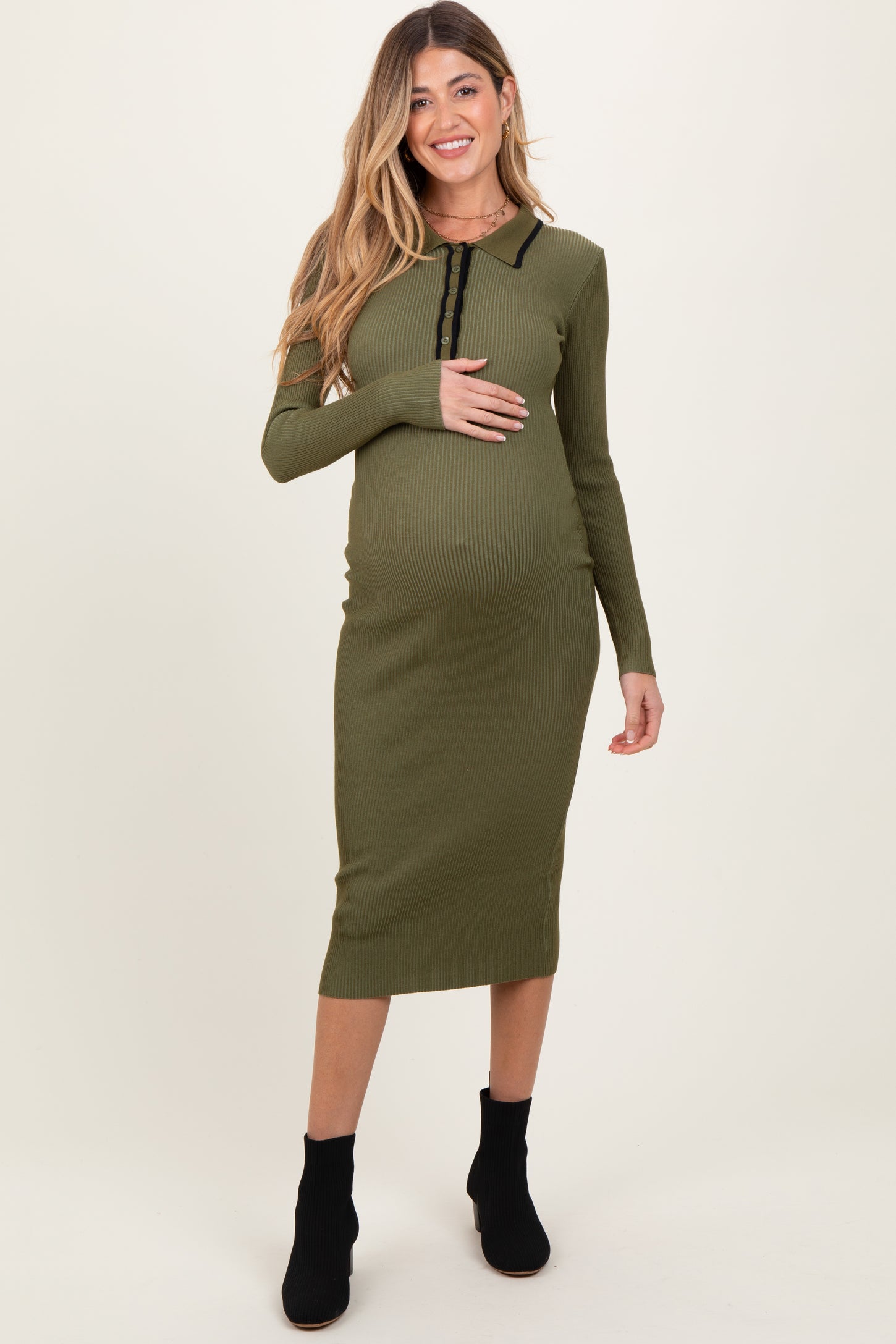 woman wearing a green ribbed maternity dress with long sleeves and a front button detail, holding her baby bump