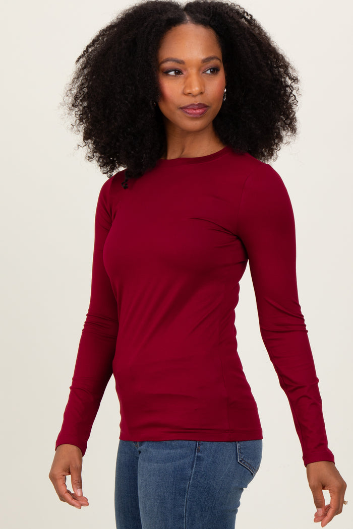 woman wearing a burgundy long sleeve fitted top paired with blue jeans
