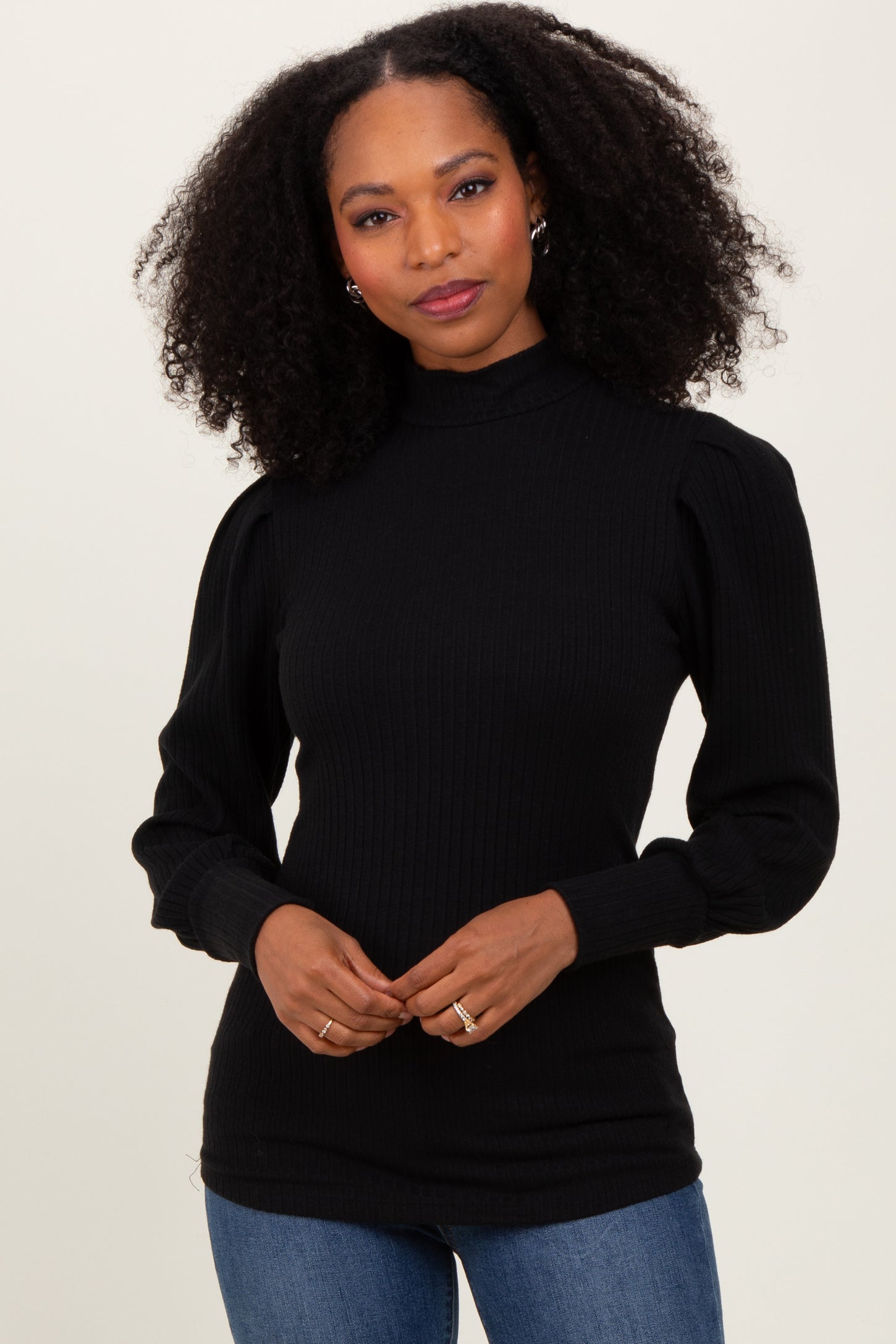woman wearing a black ribbed turtleneck sweater with puff sleeves and paired with blue jeans