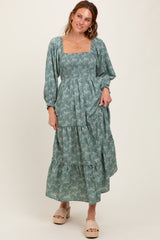woman wearing a teal floral maxi dress with square neckline and puff sleeves, standing with a smile