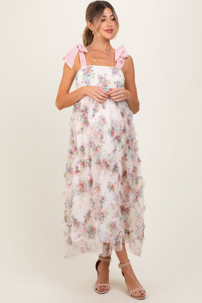woman wearing a floral maternity dress with pink bow straps and tiered ruffles, showcasing a baby bump