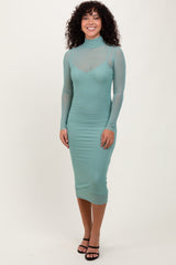 woman wearing a mint green long sleeve sheer dress with a fitted silhouette and a turtleneck collar.