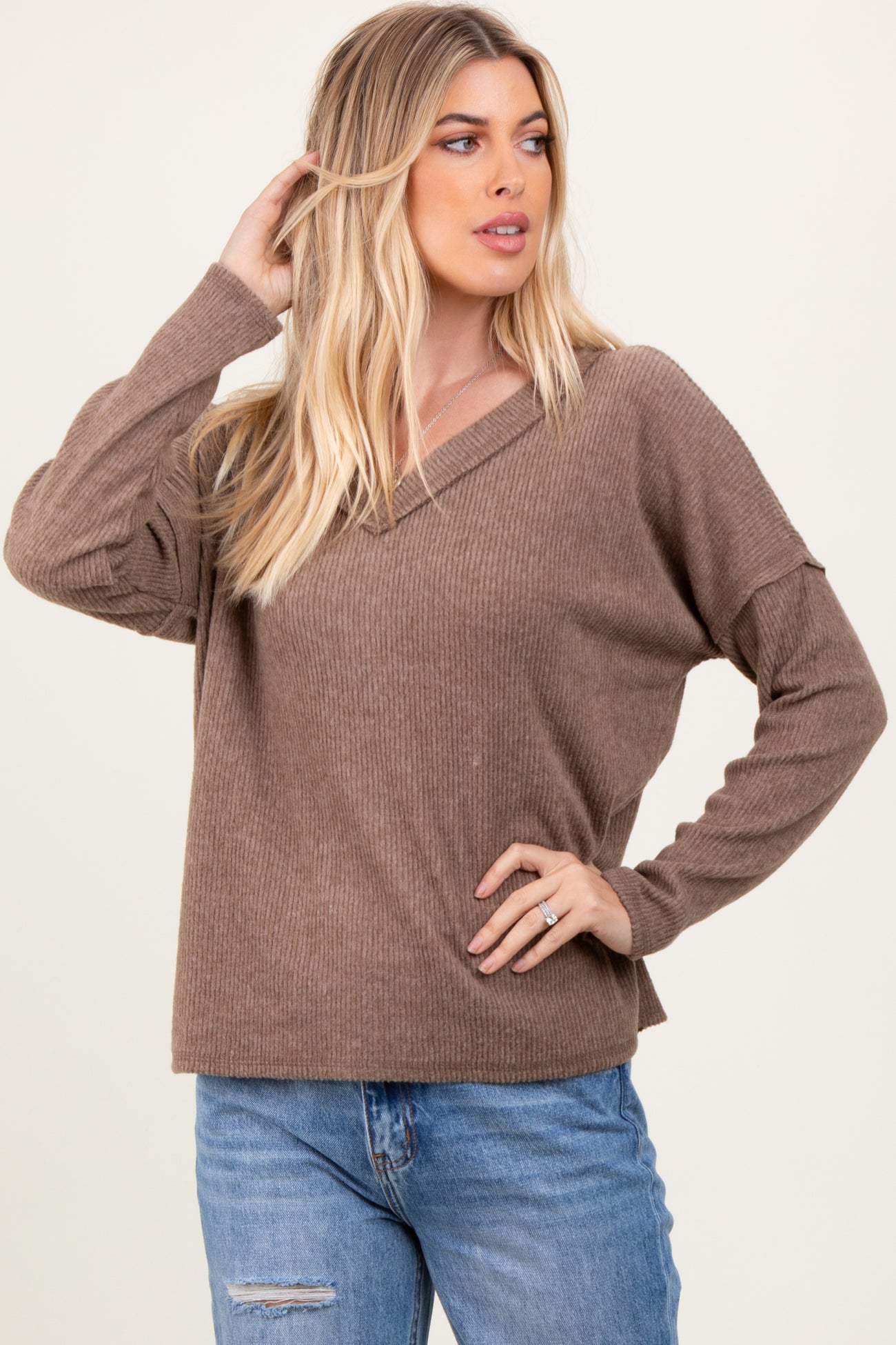 woman wearing a taupe ribbed long sleeve top with a v-neck and relaxed fit paired with light blue distressed jeans