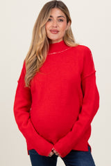 woman wearing a red oversized maternity sweater with a mock neck and visible baby bump