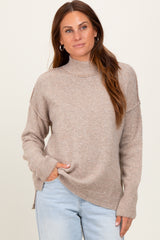woman wearing a beige high neck sweater with side slits and long sleeves, styled with light blue jeans