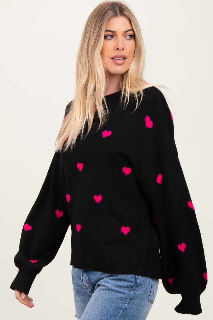 woman wearing a black sweater with pink heart patterns and balloon sleeves, styled with blue jeans