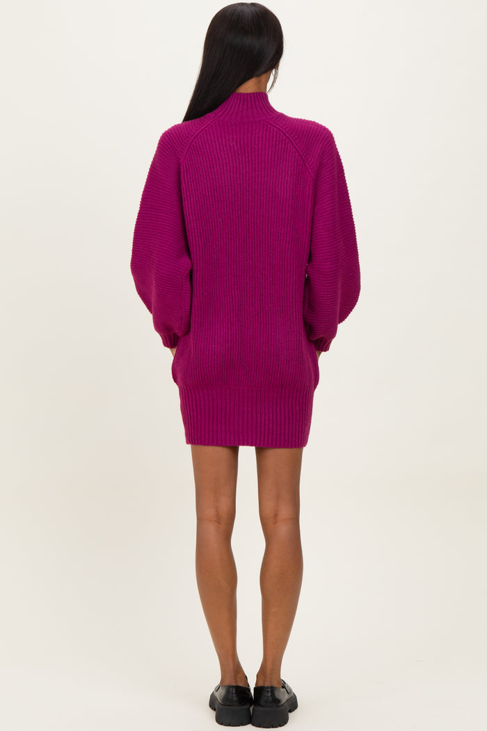 woman wearing a fuchsia oversized sweater dress with long sleeves and a high collar, viewed from the back