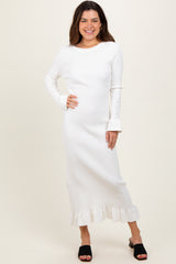 woman wearing a white ribbed long sleeve dress with flared cuffs and a ruffled hemline, styled with black slide sandals