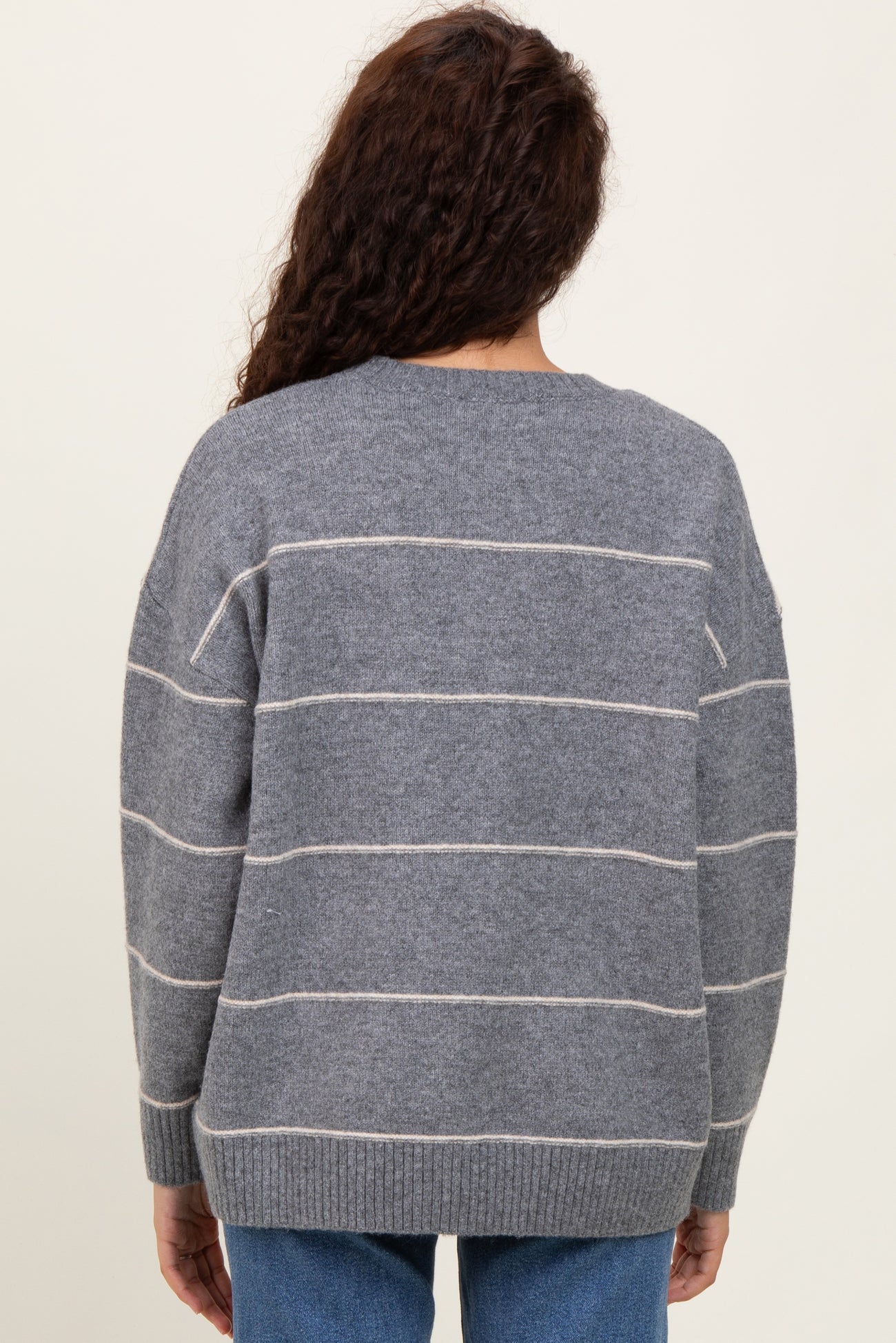 woman wearing a gray striped oversized sweater with a soft knit texture, viewed from the back