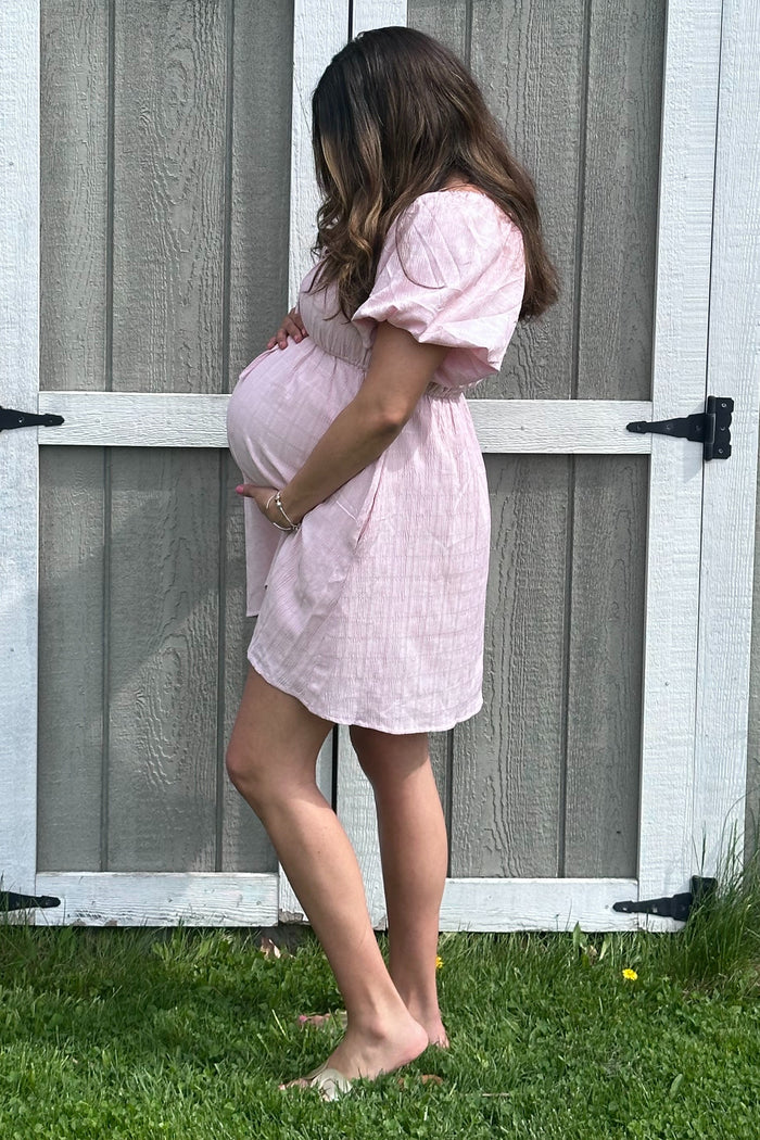 woman wearing a pink short sleeve maternity dress, showcasing her baby bump against a rustic background