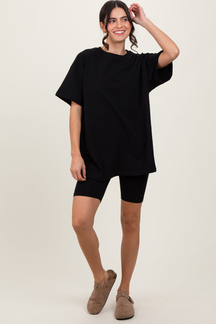 woman wearing a black oversized t-shirt and black bike shorts, standing and smiling with one hand in her hair